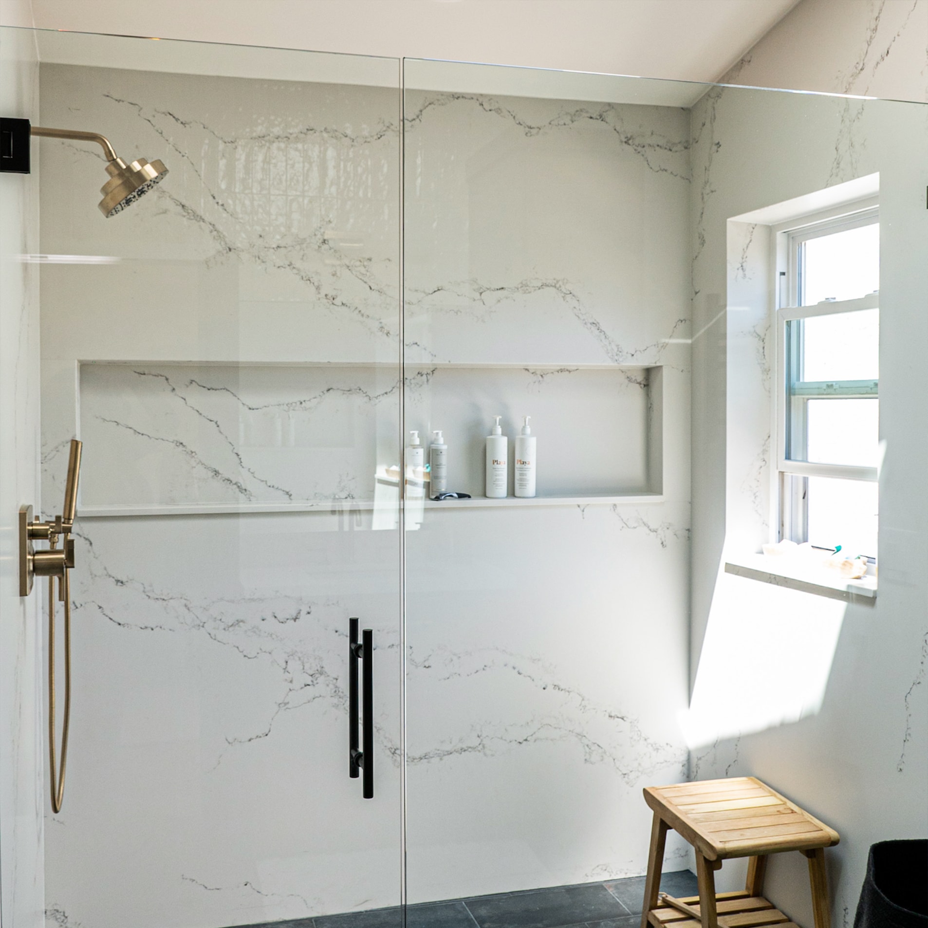 A bright marble shower with brass fittings and a wooden bench